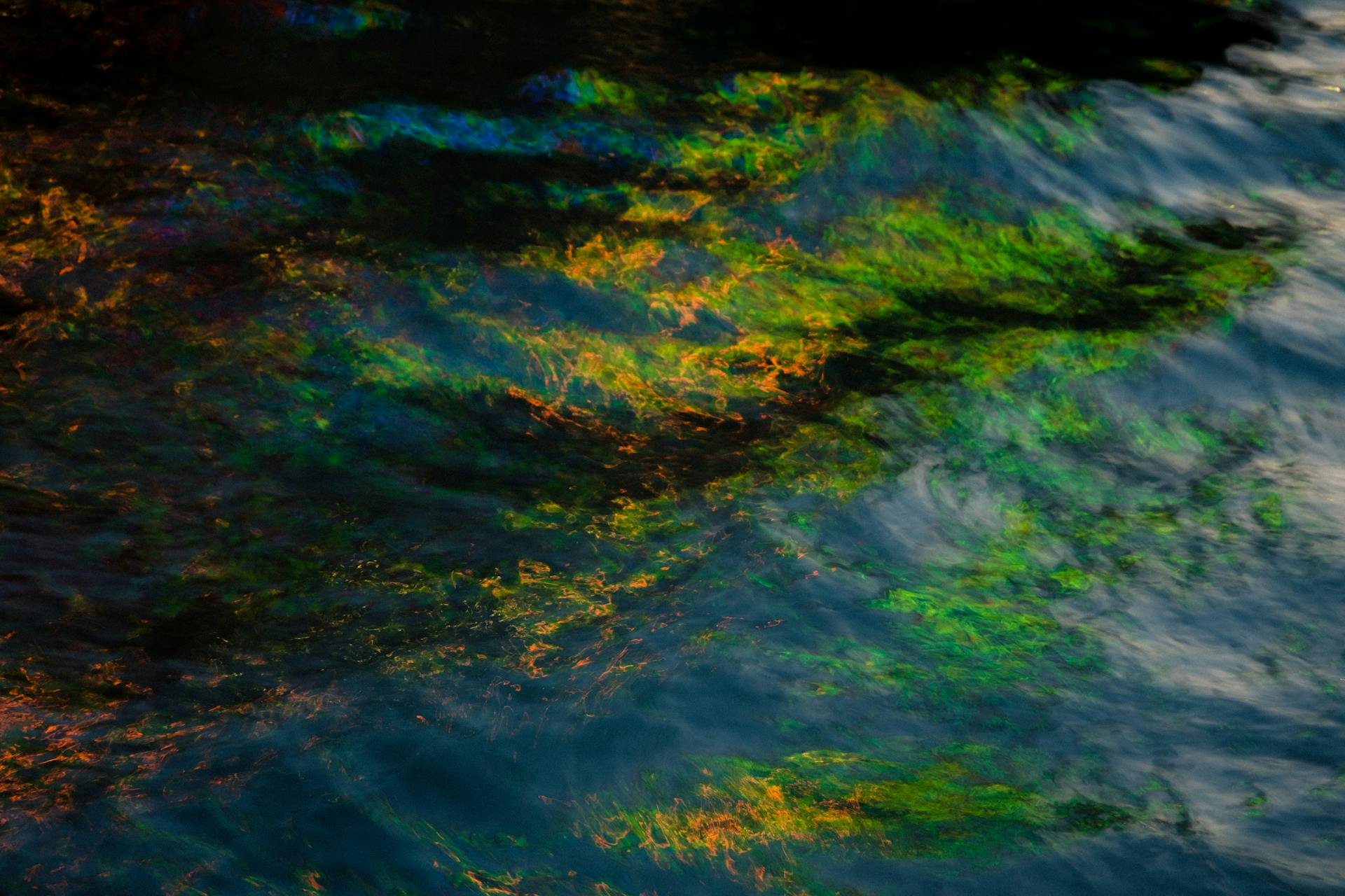 A mesmerizing abstract pattern of vibrant colors reflecting on a water surface, resembling an oil spill.