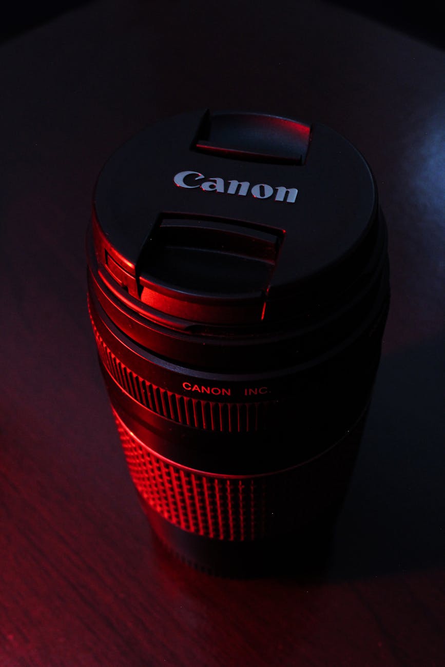 Moody close-up of a Canon camera lens set against a dark background with red accent lighting.