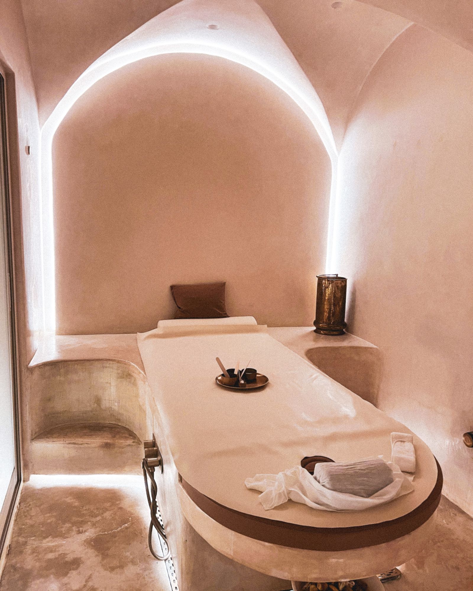 Softly lit private treatment room with arched plaster walls and a made-up waxing bed