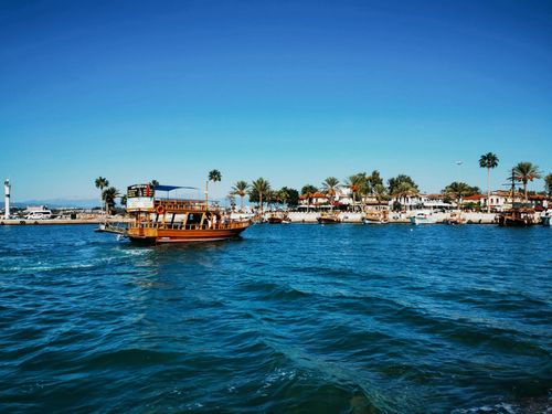 Free A traditional wooden boat sails near a palm-lined harbor on a sunny day, offering a tropical view. Stock Photo