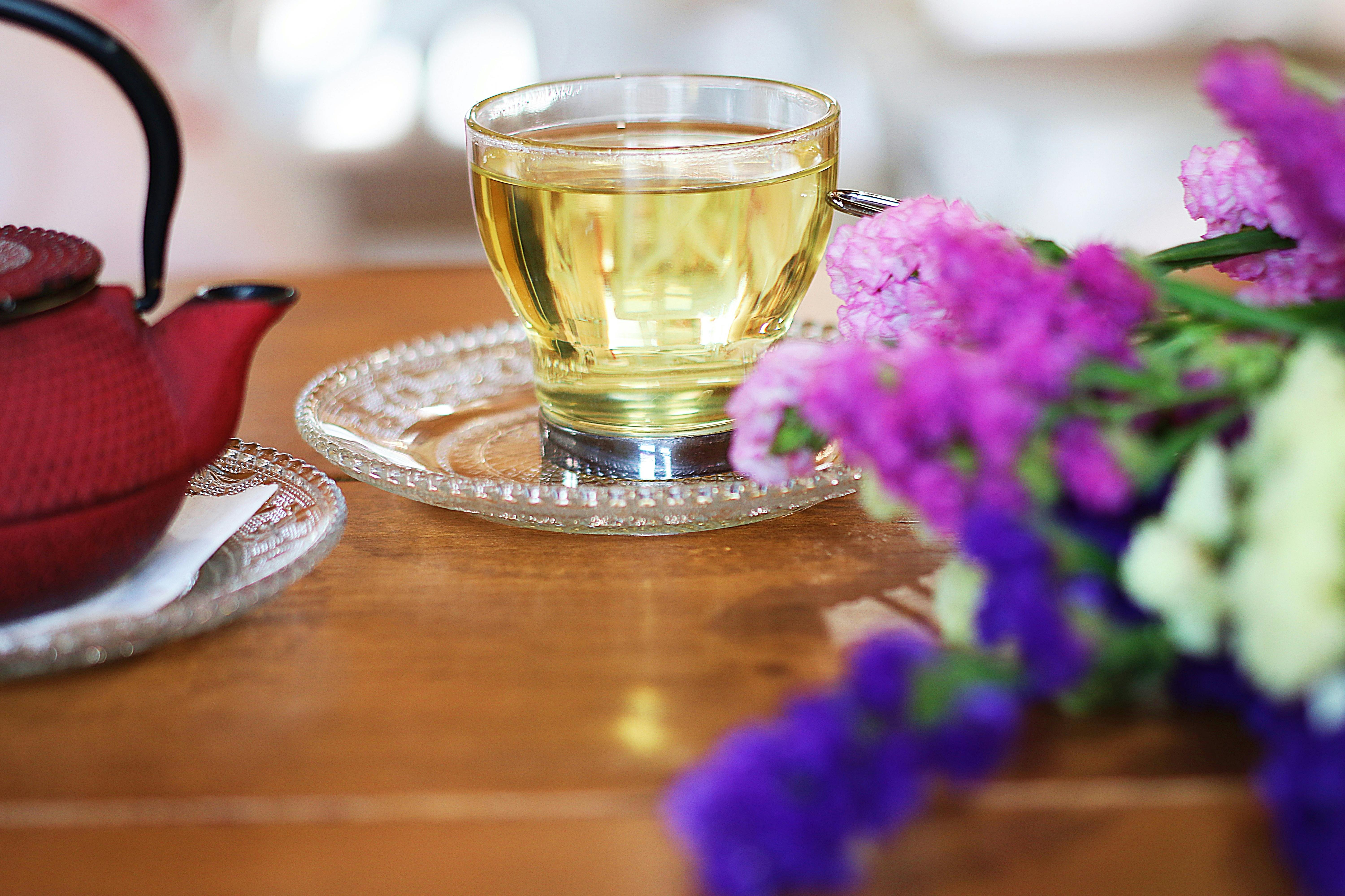 A warm cup of tea with a teapot and colorful flowers on a wooden table, capturing a serene moment.