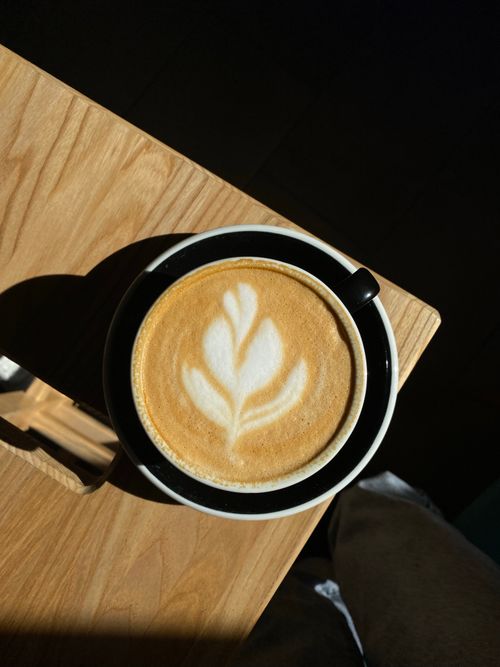 Free Cappuccino with creative latte art served in a black mug on a sunny wooden table. Stock Photo