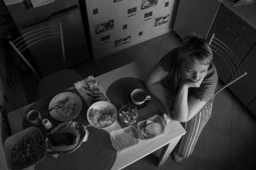 Monochrome view of a woman sitting at a kitchen table with breakfast items.