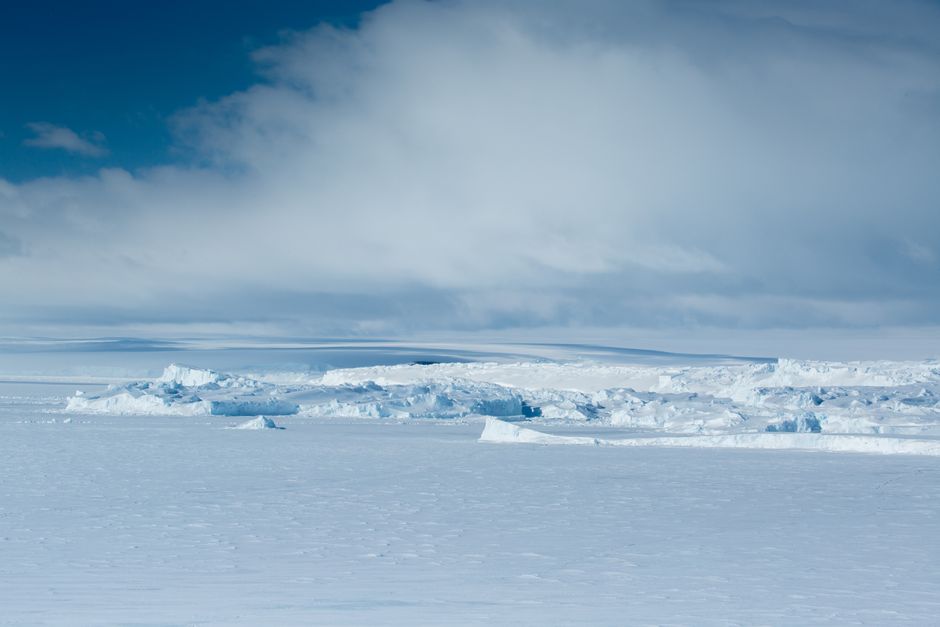 Expansive frozen scene with icy surfaces under a dramatic cloudy sky.