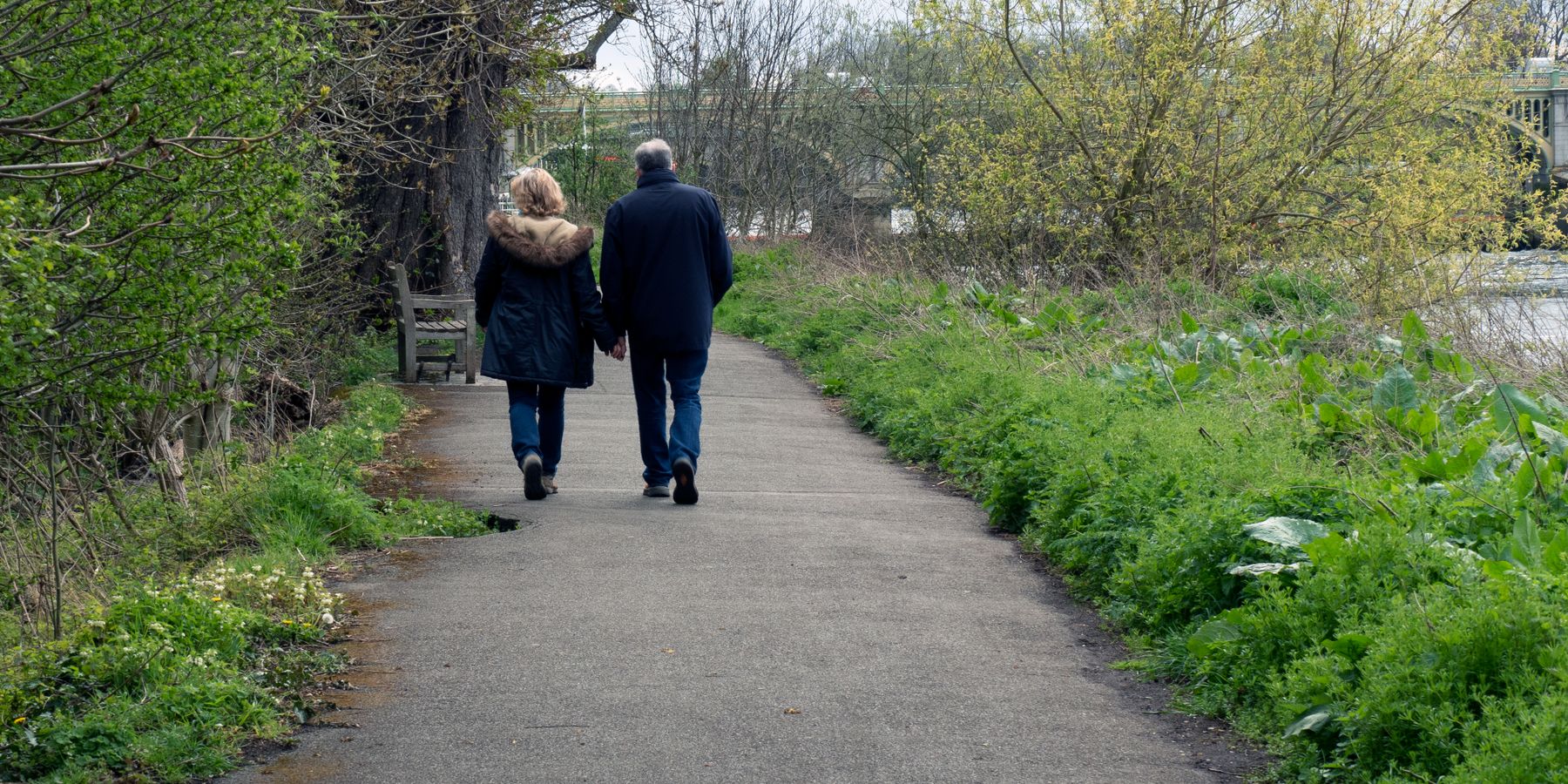 A senior couple strolls hand in hand along a peaceful park path in Hounslow, England.