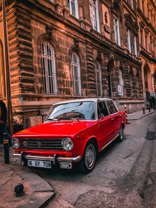 Free Red vintage car parked beside a historic building on a city street, showcasing classic automotive design. Stock Photo