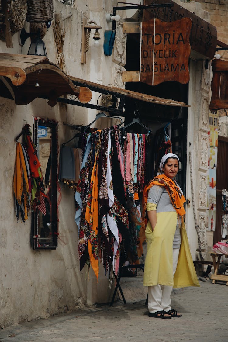 A Vendor Standing On The Side Of The Street Beside Hanging Scarfs