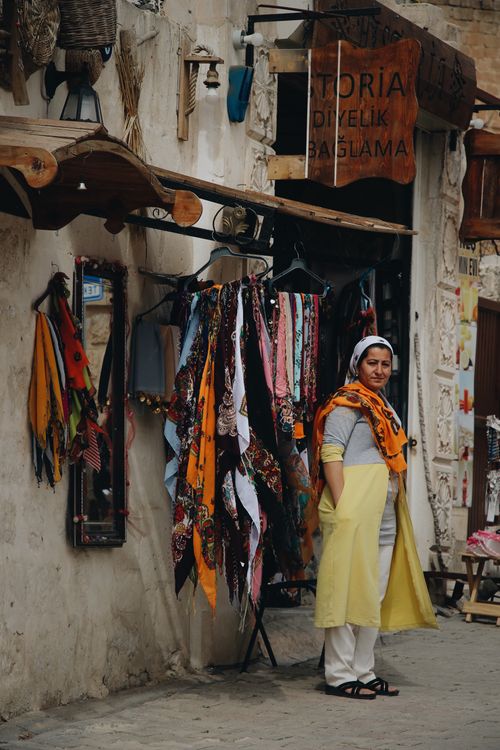 Free A woman street vendor stands by her vibrant scarf display in an outdoor marketplace. Stock Photo