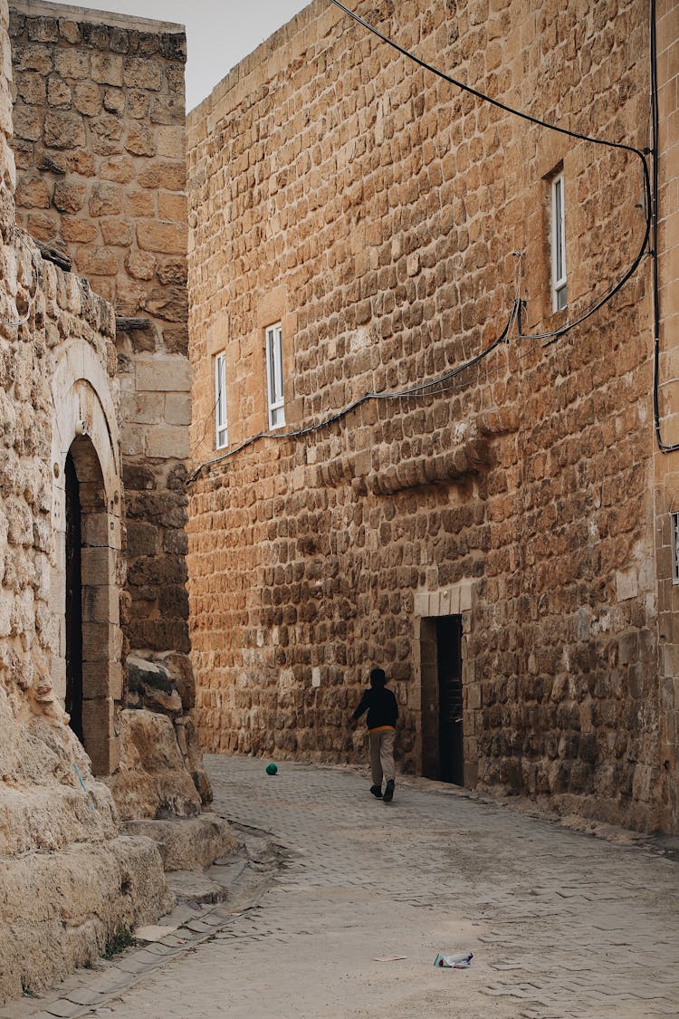 A Person Running On A Narrow Street Between Ancient Houses