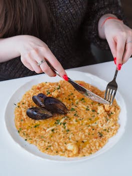 A close-up of a woman dining on seafood risotto with mussels, highlighting gourmet cuisine.