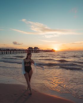 Woman in swimsuit walking on Naples beach at sunset, elegant and serene.