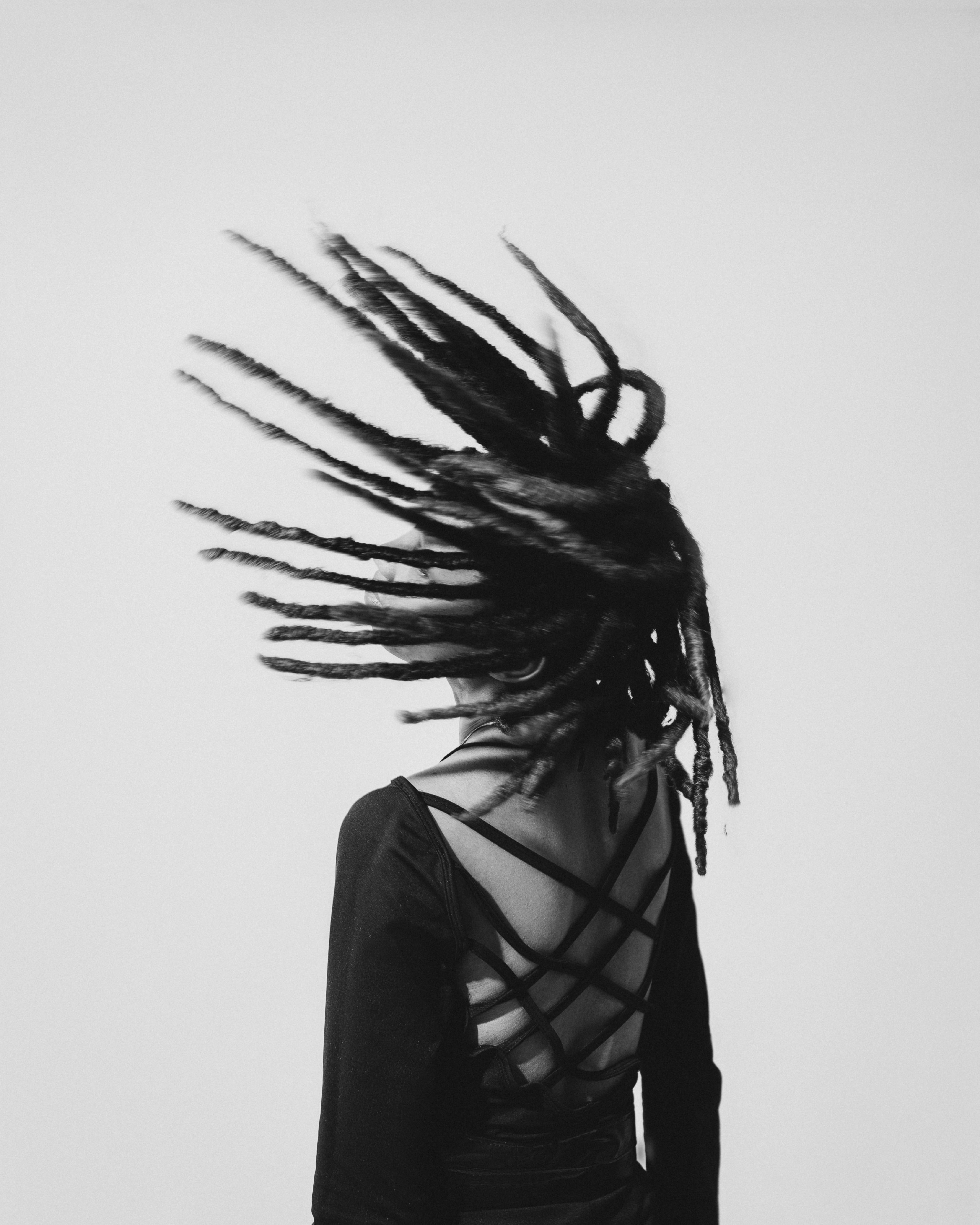 Artistic black and white photo of a person with dreadlocks flipping hair, highlighting movement and style.