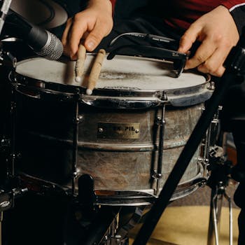 Close-up shot of a drummer playing a snare drum with drumsticks in a music studio.
