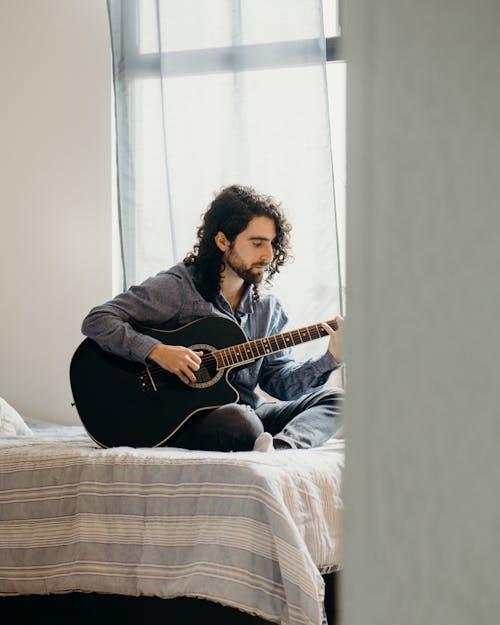 Man sitting on Bed playing an Acoustic Guitar 