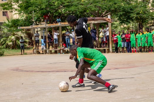 Two players compete fiercely in a community soccer game in Cacuaco, Luanda, watched by a local crowd.
