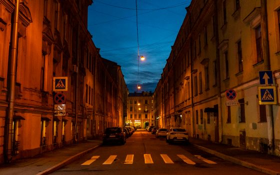 Quiet street in St. Petersburg with warm lighting and parked cars, set against a deep blue night sky.