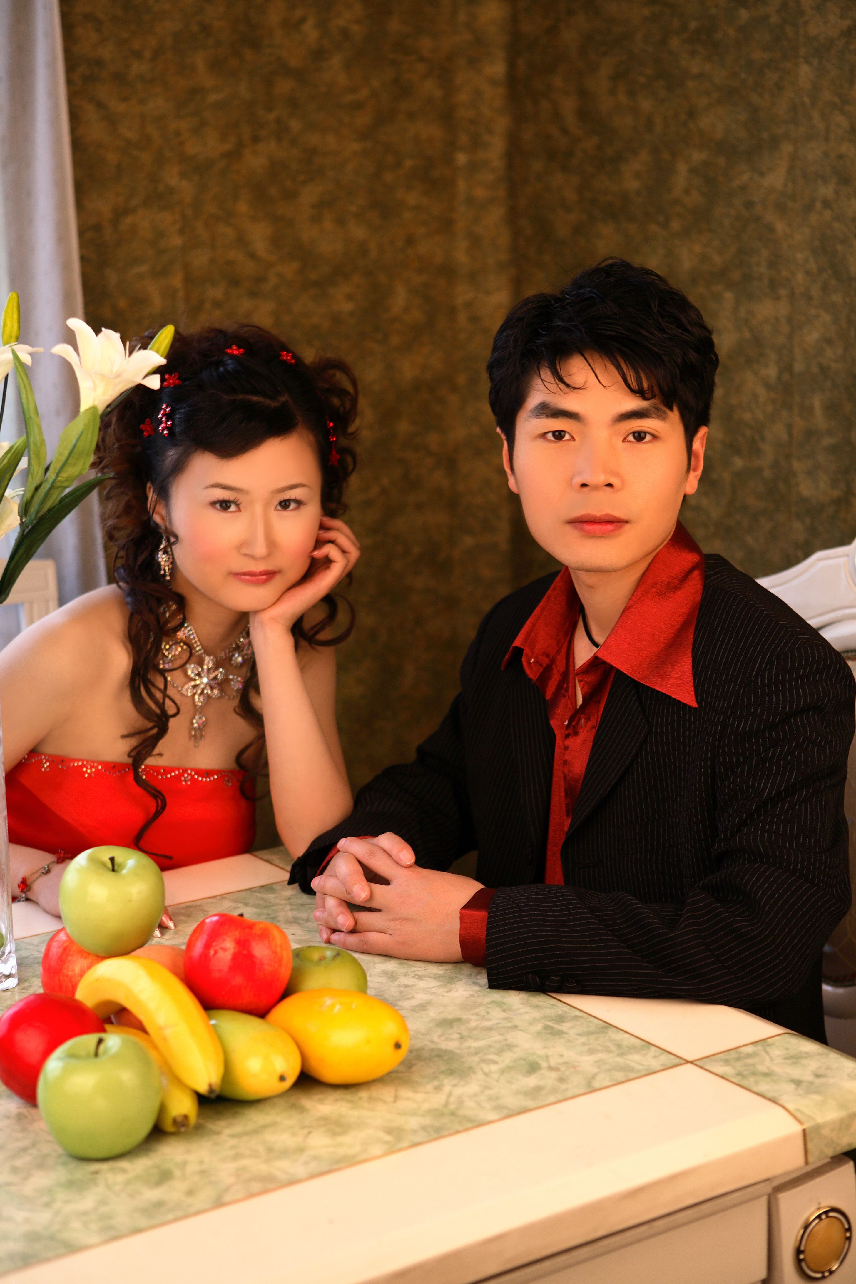 Stylish couple sitting at a table with fruits indoors, showcasing elegance and togetherness.