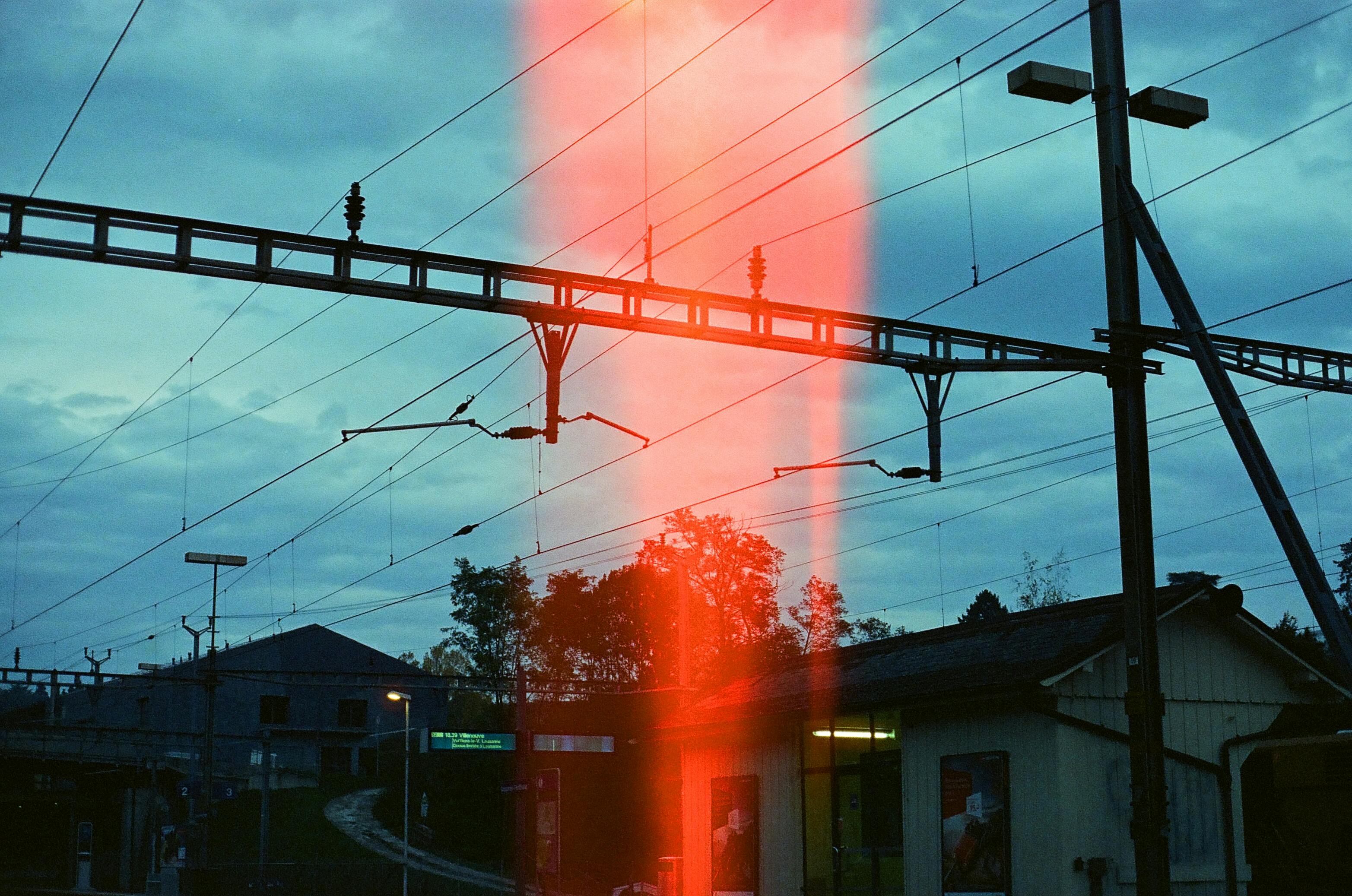 Train station with electric lines at dusk featuring light leak and industrial elements.