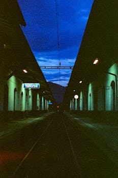 A captivating night view of Vallorbe train station, showcasing illuminated platforms and a deep blue sky.