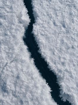Close-up view of a crack in a frozen surface covered with snow, showcasing winter textures.