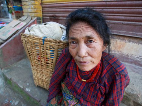 A middle-aged woman in traditional attire sits beside a woven basket on outdoor steps.