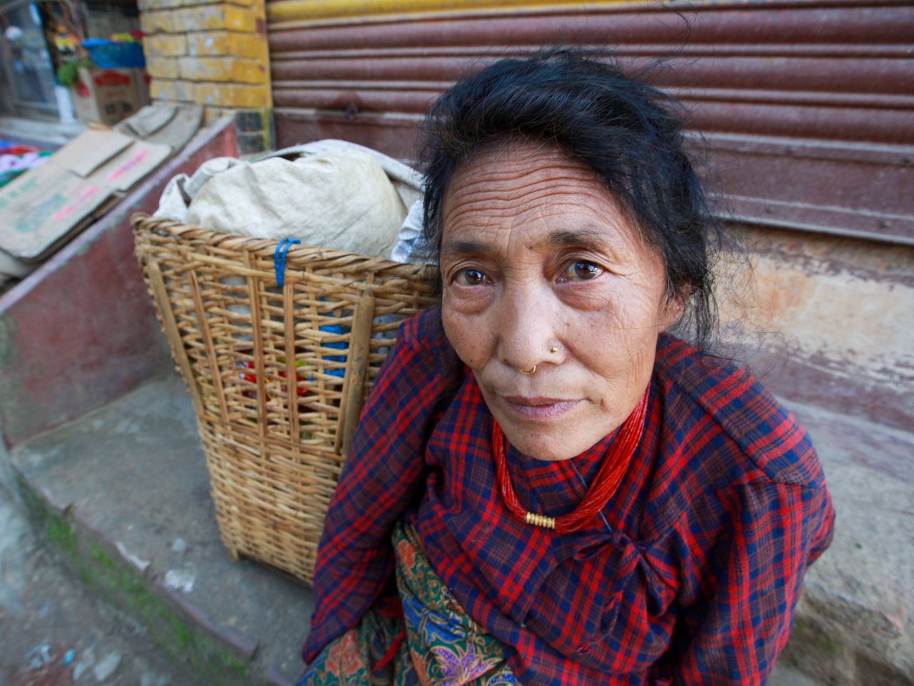 a middle aged woman in traditional attire sits beside a woven basket o
