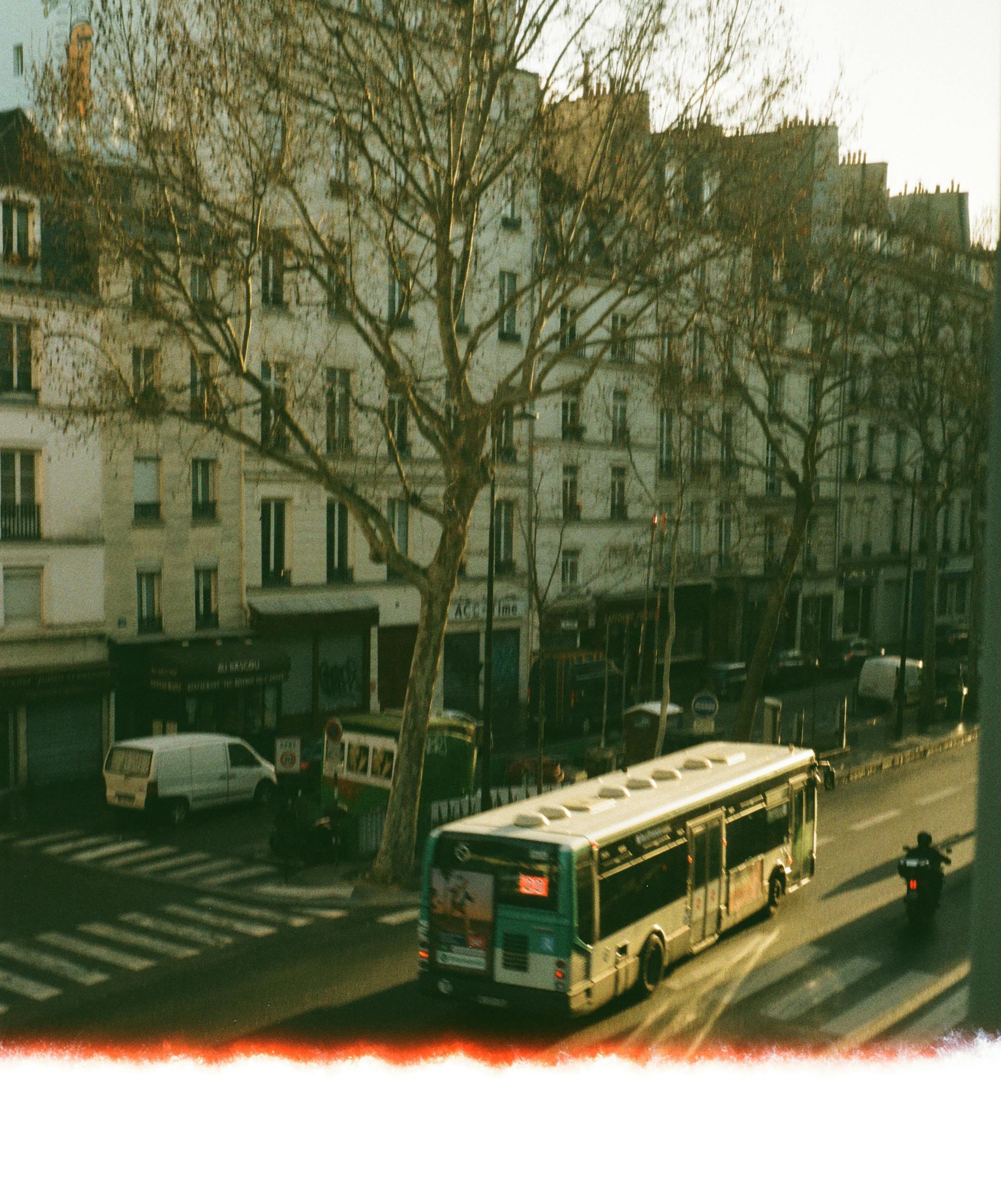 High angle view of a street in Paris featuring a bus, buildings, and trees during the day.