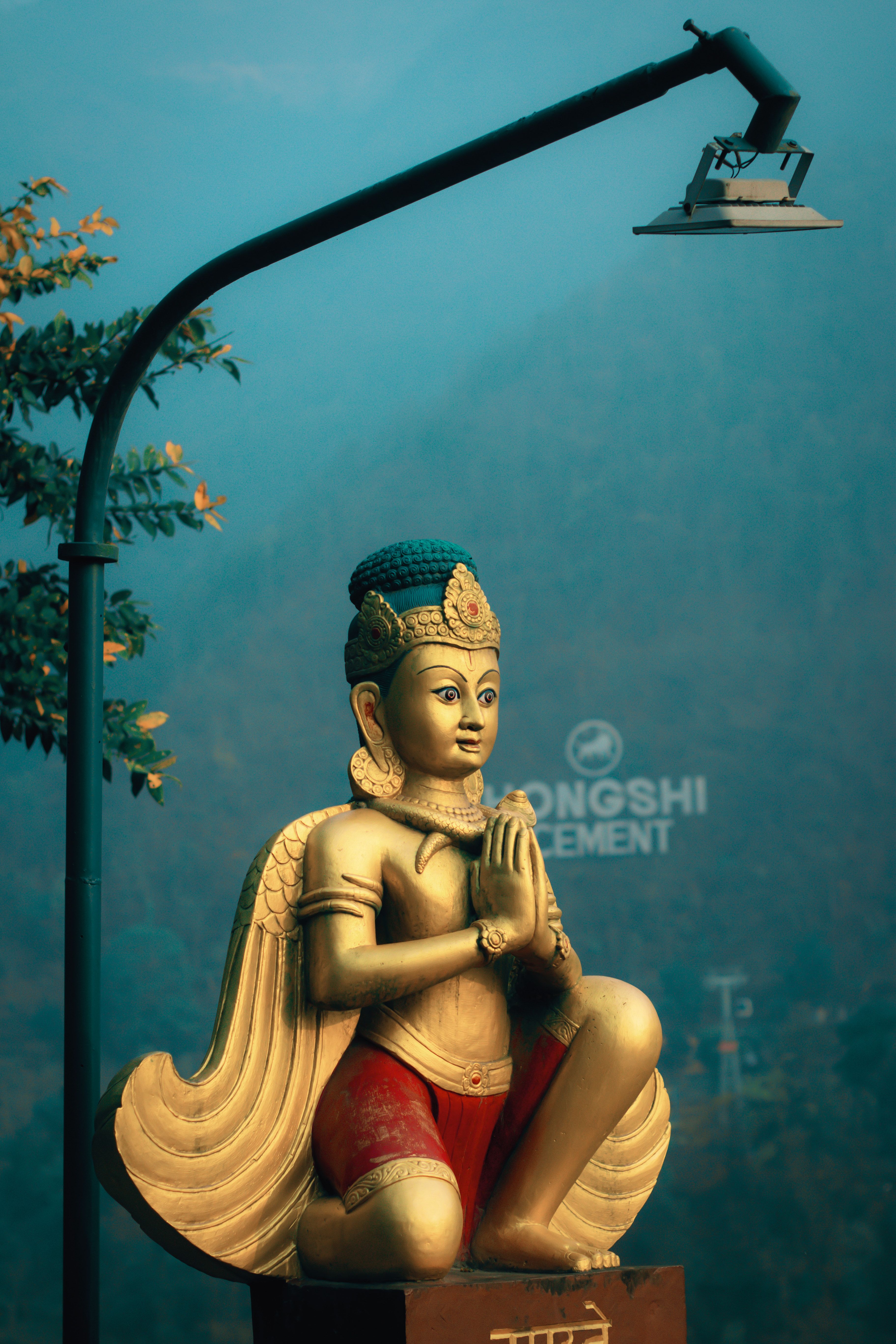 Golden statue of a Buddhist figure in prayer near a decorative lamppost outdoors.