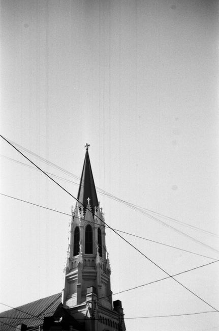 A monochrome photo of a church steeple with intersecting wires against a clear sky.