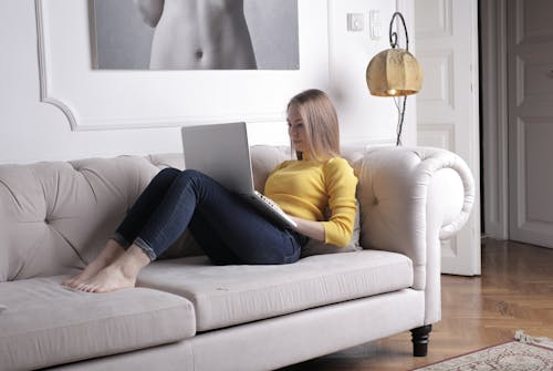 Woman in Yellow Long Sleeve Shirt and Blue Pants Sitting on White Couch