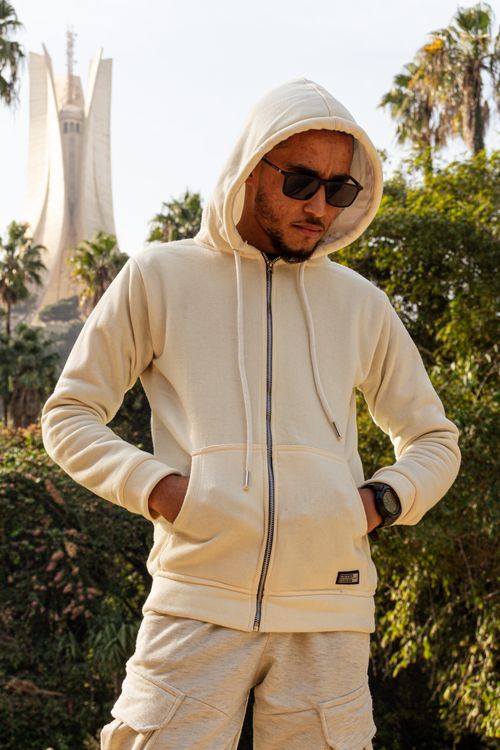Free Stylish young man in sunglasses and hoodie posing in Algiers with iconic monument in the background. Stock Photo