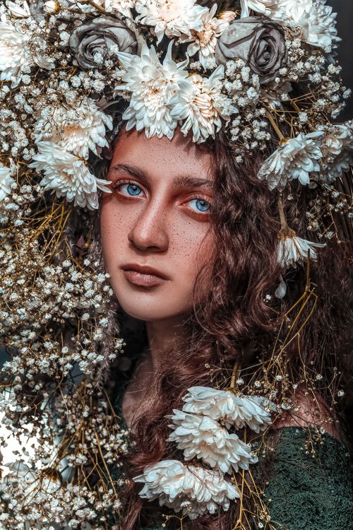 Free Captivating close-up of a woman with striking blue eyes surrounded by a floral crown, artfully captured. Stock Photo