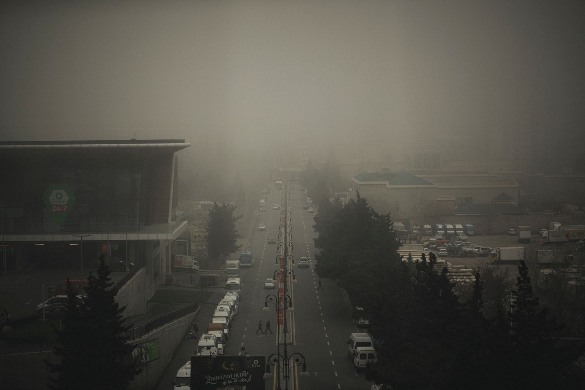 A hazy urban street lined with multi-story buildings on a gloomy, overcast day.