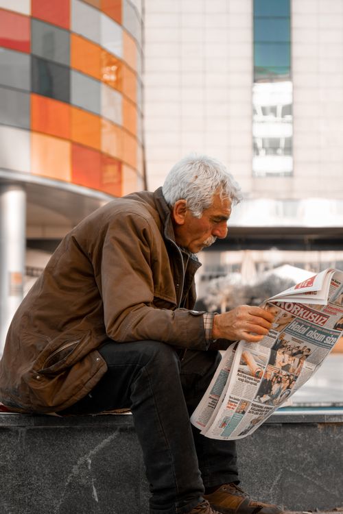 Free Senior man with white hair reading newspaper outside urban building Stock Photo