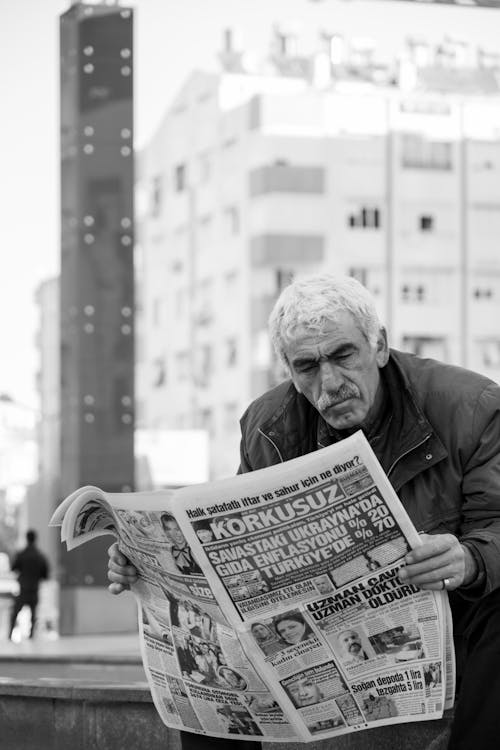 Grayscale Photo of an Elderly Man Reading Newspaper