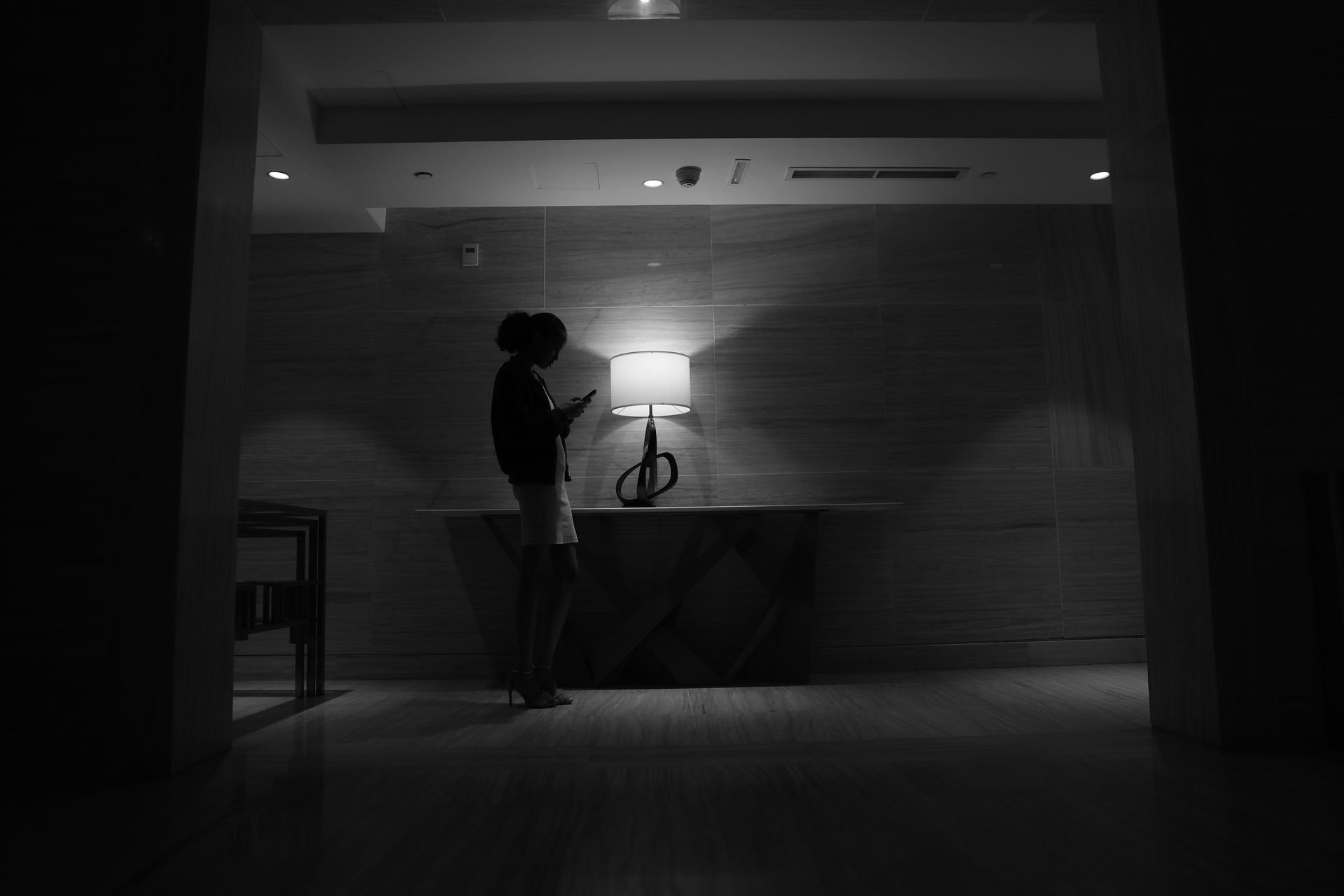Silhouette of a woman using a phone in a modern urban setting. Moody black and white photography.