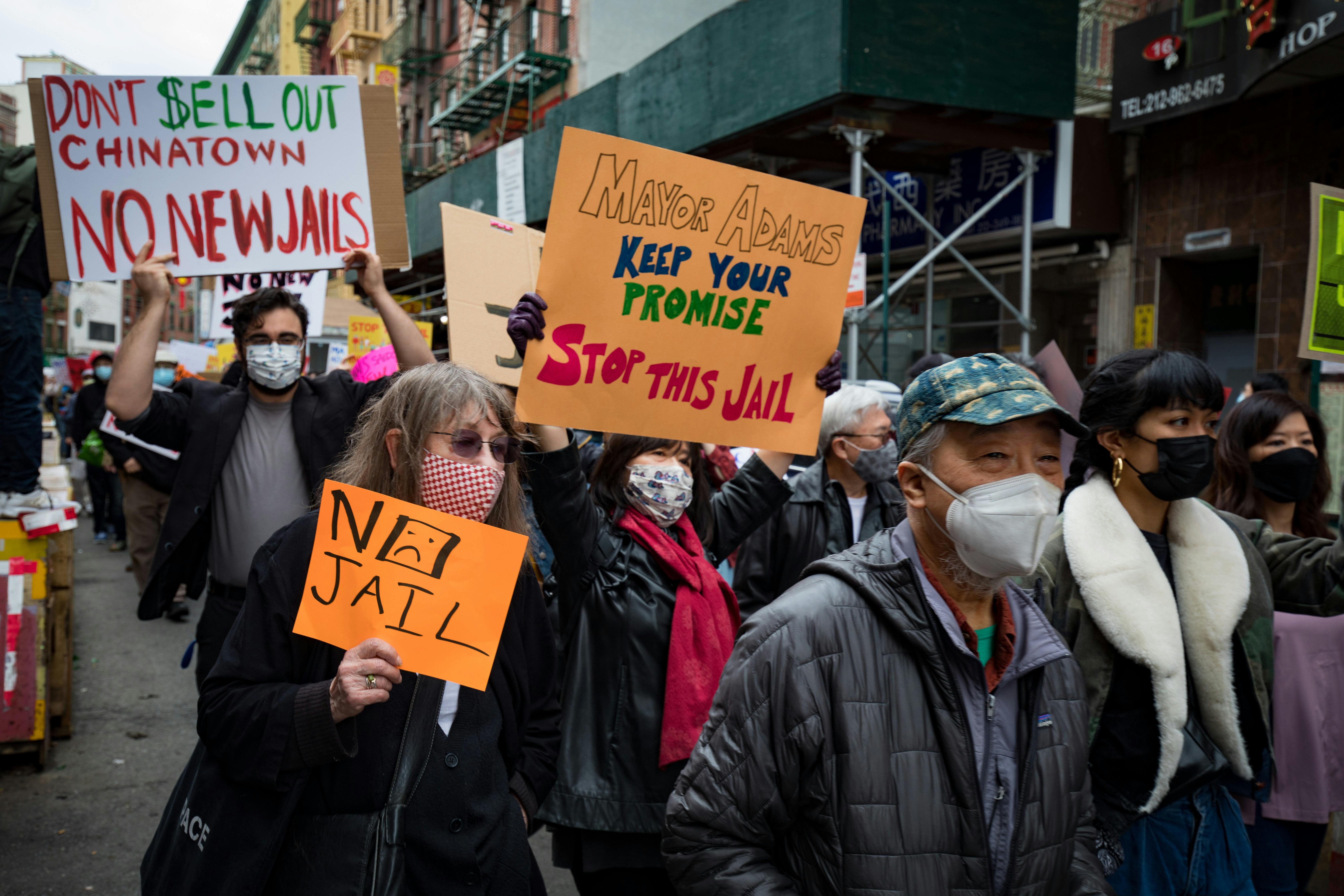 Protesters rally in Chinatown NYC against new jail plans, holding signs and placards.