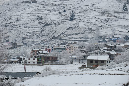 Serene winter landscape of a small town covered in snow under a mountainous backdrop.
