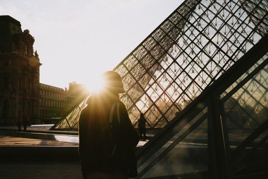 Silhouette of a person near the Louvre Pyramid during sunrise in Paris, France.