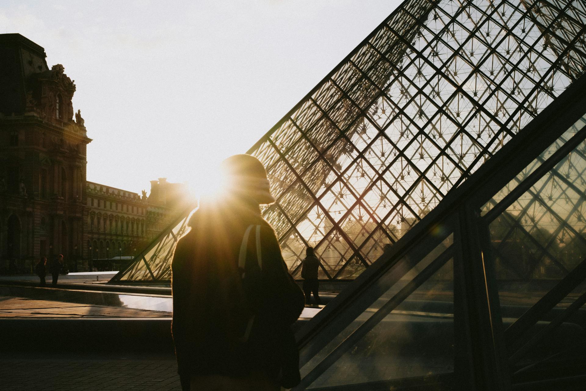 Silhouette of a person near the Louvre Pyramid during sunrise in Paris, France.