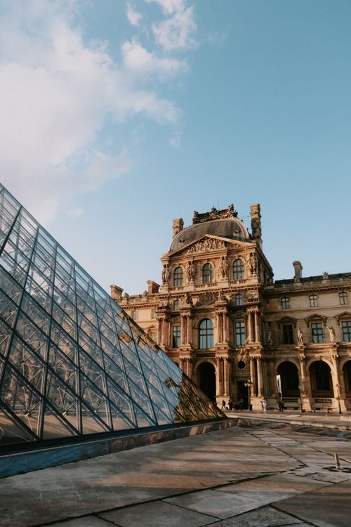 Free Louvre Pyramid and historic palace facade under a blue sky in Paris. Stock Photo