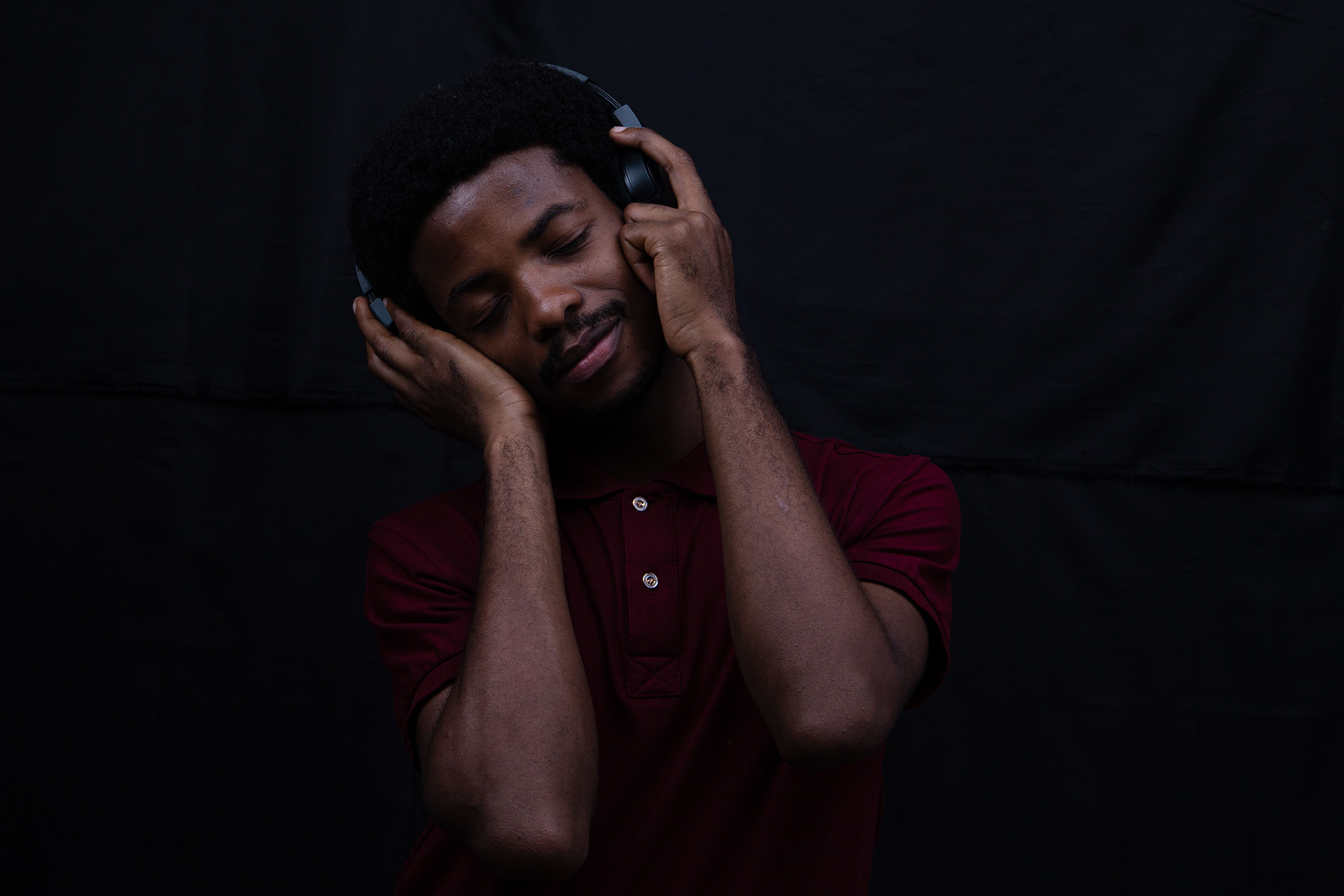 Man with eyes closed listening through over-ear headphones in a red polo shirt