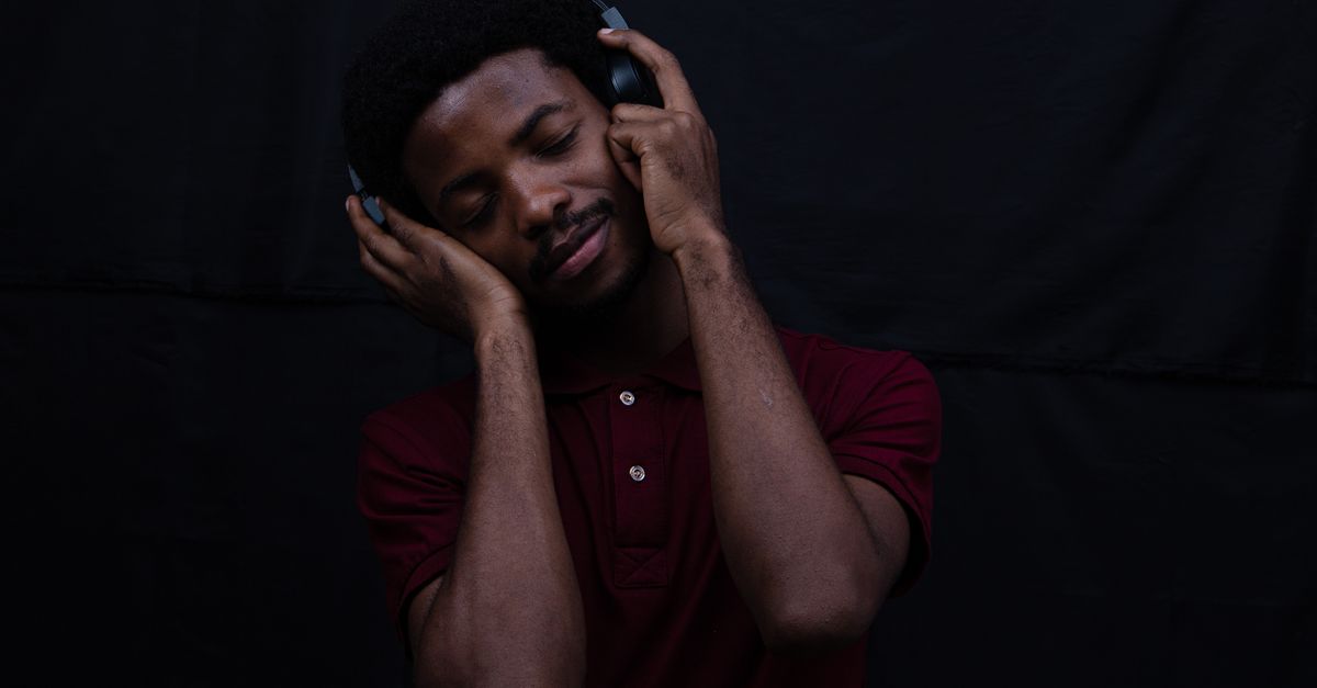 Man with eyes closed listening through over-ear headphones in a red polo shirt