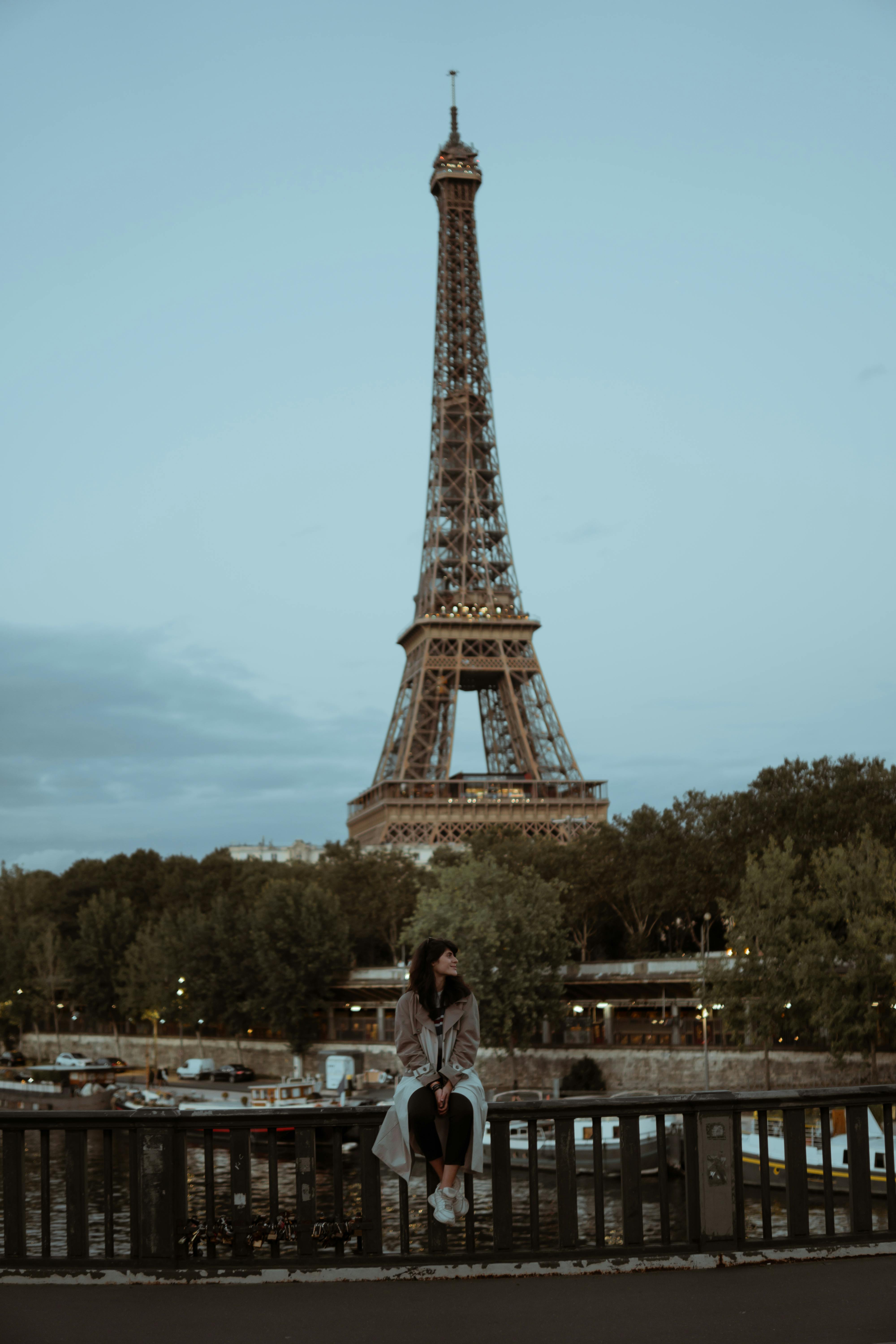 woman sitting on a bridge fence in front of the eiffel tower