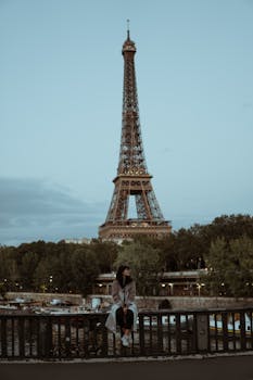 A woman sitting on a bridge with the Eiffel Tower in the background at dusk, Paris, France.
