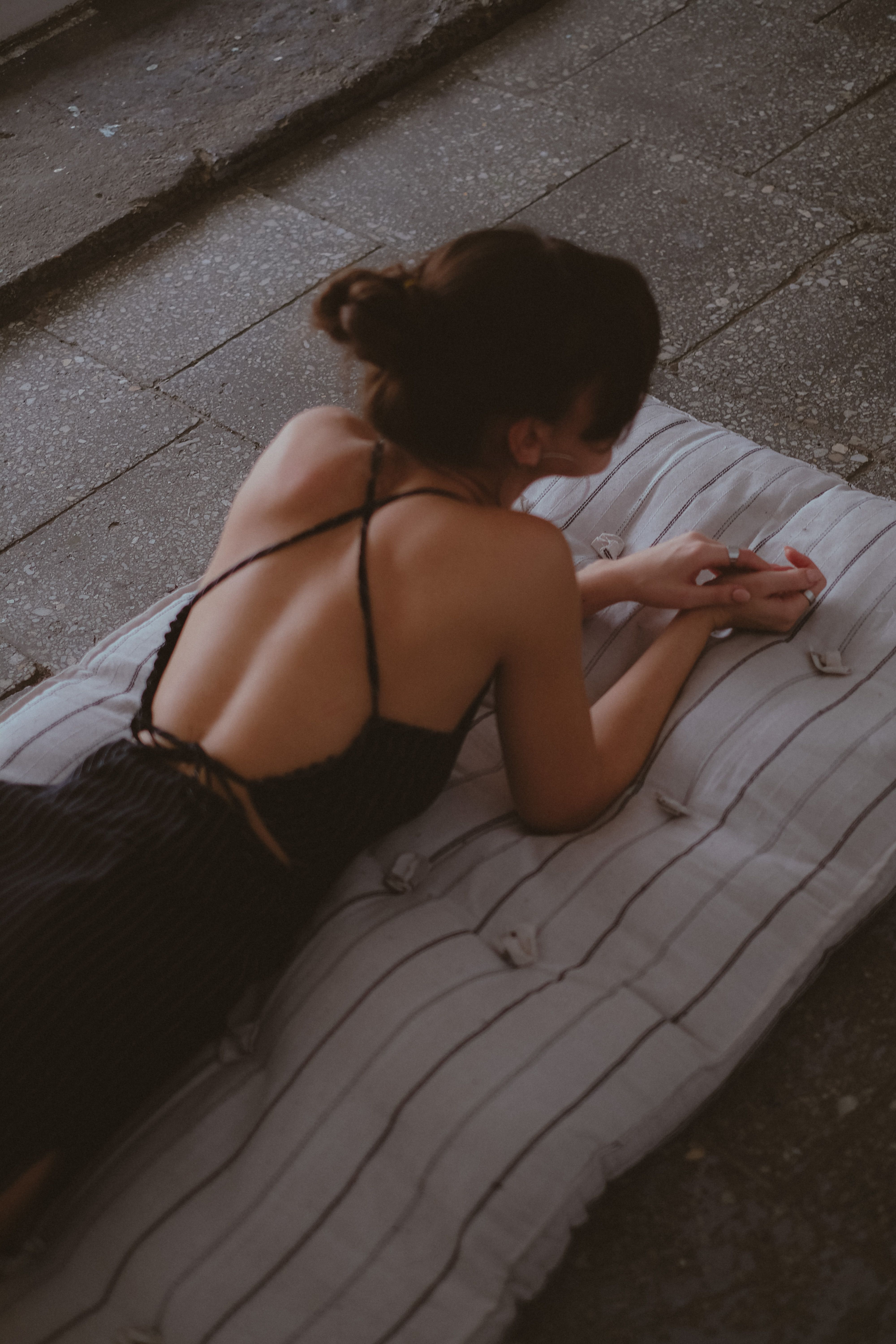 A woman in a backless black dress relaxing indoors on a striped mattress.