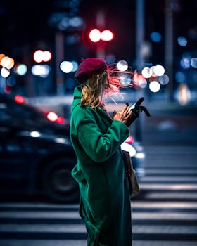 Stylish woman uses phone on Warsaw street at night, vibrant city vibes.