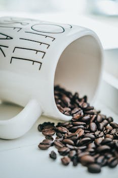 Close-up image of roasted coffee beans spilling from a white mug with text.