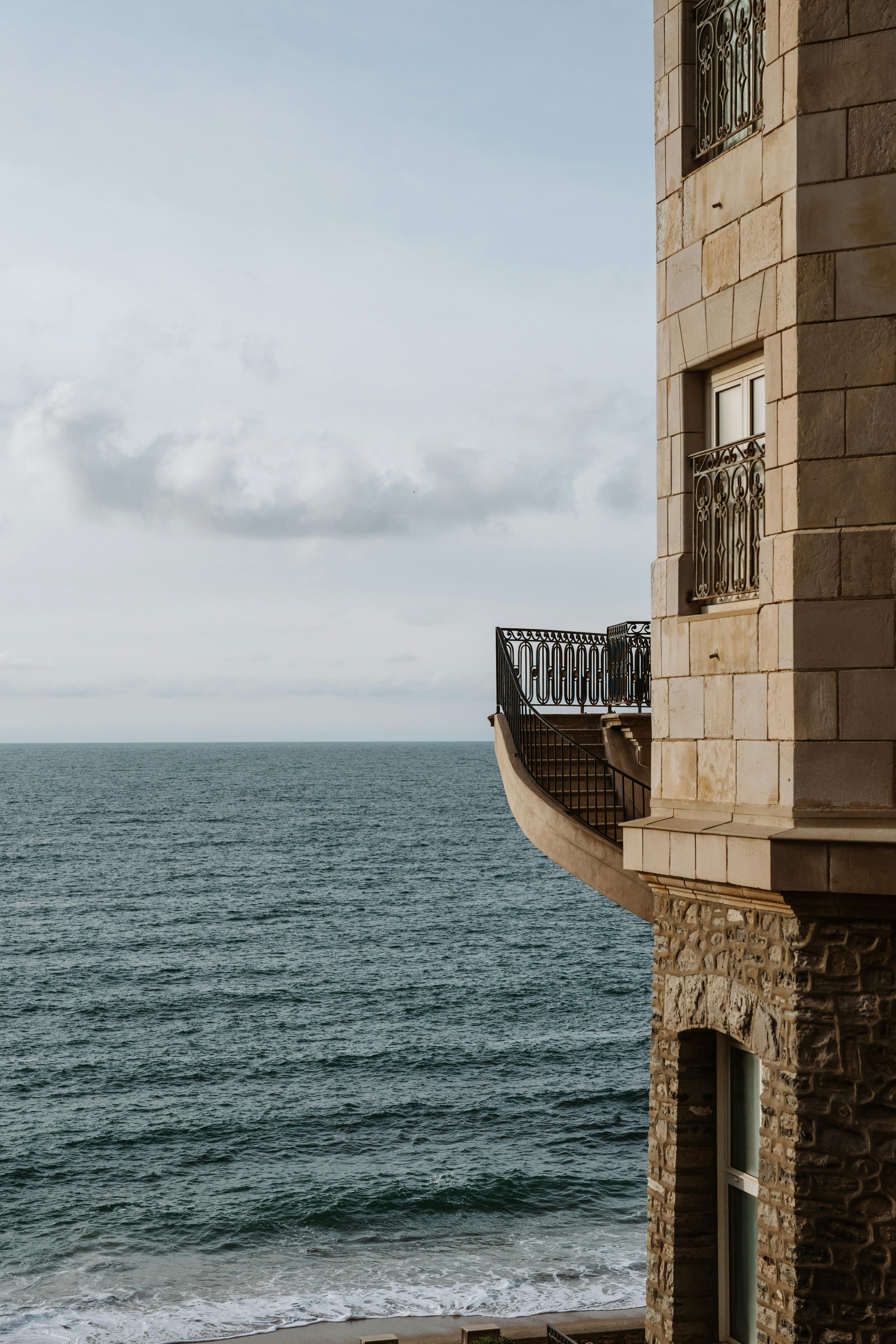 Brown stone building with ocean view in Biarritz, France. Elegant railings highlight coastal charm.