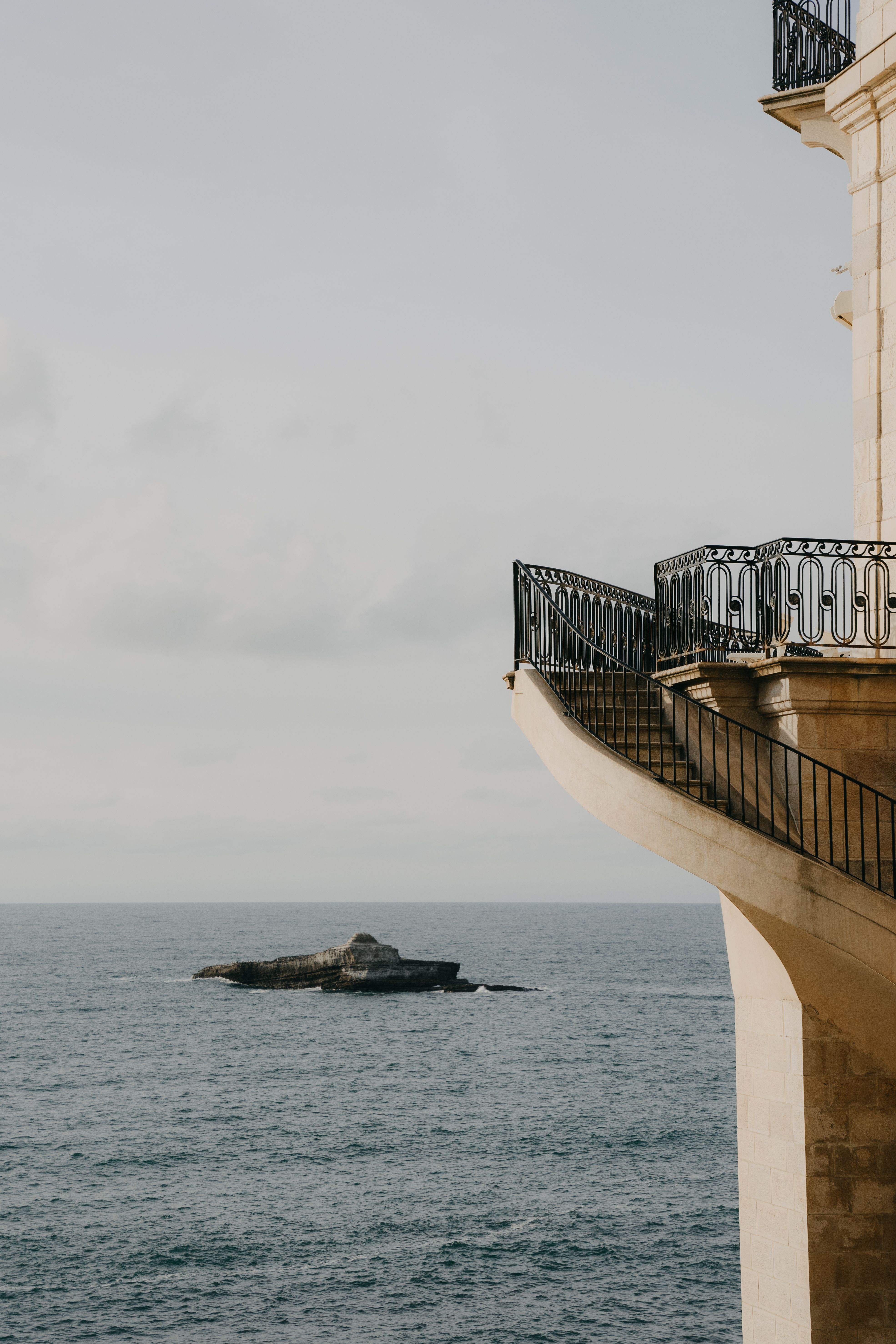 A beautiful seaside building in Biarritz with metal railings overlooking the calm ocean waters.